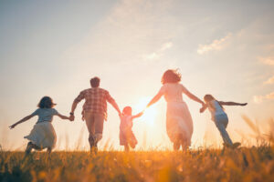 A family of five, holding hands, runs through a grassy field towards the sunset on a clear day. They are silhouetted by the sunlight, symbolizing happiness and togetherness—beautifully capturing the benefits of daily movement for building joyful memories and strong family bonds.
