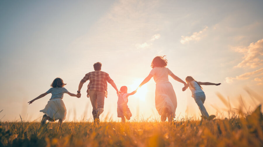 A family of five, holding hands, runs through a grassy field towards the sunset on a clear day. They are silhouetted by the sunlight, symbolizing happiness and togetherness—beautifully capturing the benefits of daily movement for building joyful memories and strong family bonds.